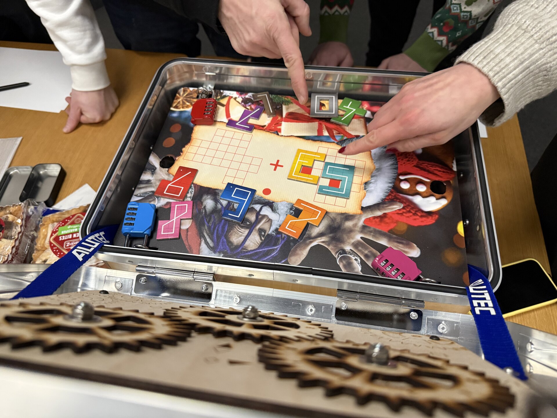 Geöffneter Beat-the-Red-Box-Koffer mit Zahnrad-Mechanik im Deckel, Teilnehmer zeigen auf ein Rätsel
